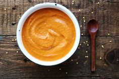 a white bowl filled with sauce next to a spoon on top of a wooden table