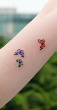 a woman's arm with three colorful butterflies on the left side of her arm