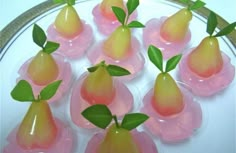 pears with green leaves are arranged in pink plastic cups on a white and gold plate