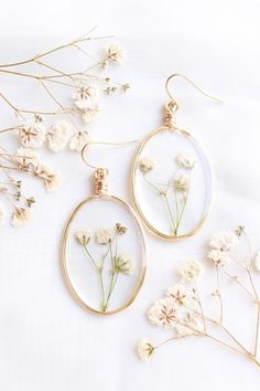 two white flowers are sitting in glass hoop earrings on a white surface with gold wire