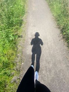 a person standing on a dirt road with their shadow in the air and grass behind them