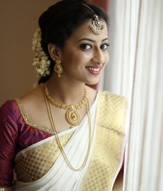 a woman in a white and gold sari with jewelry on her neck, smiling at the camera