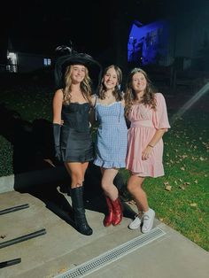 three girls are posing for the camera in front of a house at night with their hats on