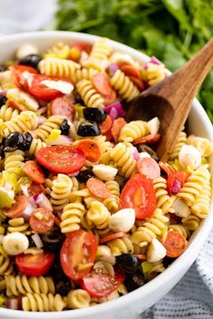 a white bowl filled with pasta salad and a wooden spoon