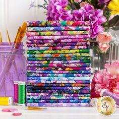 a stack of multicolored fabric next to some flowers and scissors on a table