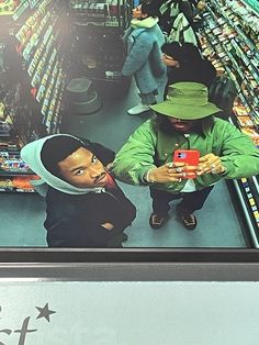 two men are looking at their cell phones in a store aisle while another man looks on