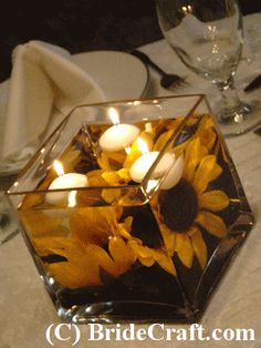 sunflowers and candles in a square glass vase on a table with white linen