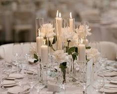 white flowers and candles sit in tall clear vases on a table set for an elegant dinner