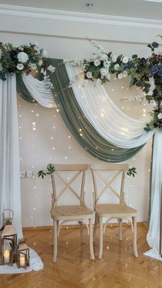 two wooden chairs sitting in front of a white drape with flowers and candles on it