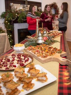 people standing around a table full of food and snacks on it's long serving trays