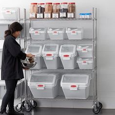 a woman standing in front of a shelf filled with containers and bins on wheels