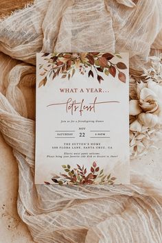 a white and brown wedding card on top of a cloth covered tablecloth with flowers