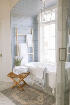 a white bath tub sitting under a window next to a rug and towel rack in a bathroom