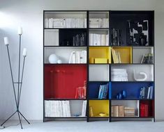 a book shelf filled with lots of different colored books next to a white wall and floor