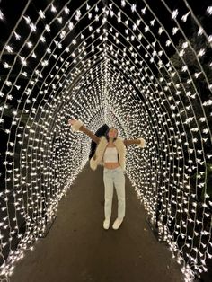 a woman standing in the middle of a tunnel covered with christmas lights