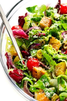 a salad with lettuce, tomatoes, and other vegetables in a glass bowl