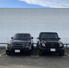 two black trucks parked next to each other in front of a white wall and fence