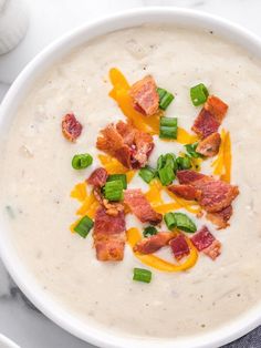 a bowl of soup with bacon, cheese and green onions in it on a marble surface