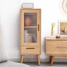 a wooden cabinet with glass doors next to a white wall and a gray chair in front of it