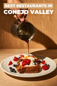 a person pouring sauce on top of a piece of bread with berries and blueberries