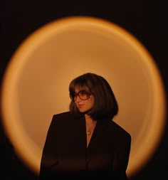 a woman wearing glasses standing in front of a circular object with light coming from it