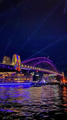 a bridge that is lit up at night with lights in the sky and water below it