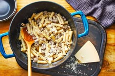 a skillet filled with pasta and cheese on top of a wooden table next to a blue spatula