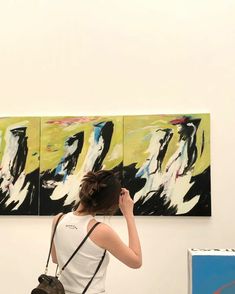 a woman standing in front of two paintings on the wall with her phone to her ear