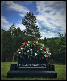 a memorial bench with flowers and greenery on it in front of a pine tree