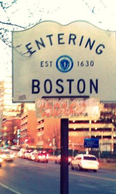 the sign for boston is lit up in the evening time, with cars driving down the street behind it