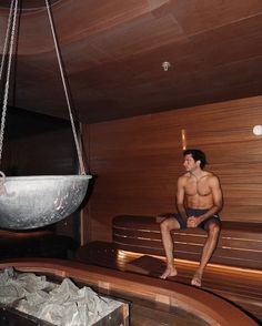 a shirtless man sitting on a bench next to a bowl hanging from the ceiling