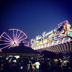 an amusement park at night with ferris wheel and fairground sign in the background as people walk around