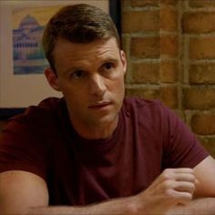 a man sitting at a table in front of a brick wall with his arms crossed