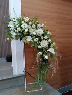 a vase filled with white flowers sitting on top of a wooden floor next to a wall