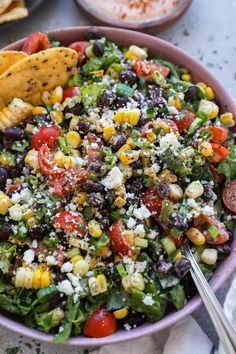 a colorful salad with corn, tomatoes, black beans and feta cheese in a purple bowl