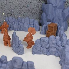 some toy figurines are standing in front of small rocks and boulders on a white surface