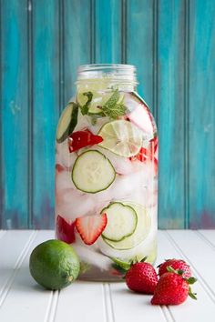 a mason jar filled with cucumbers, strawberries and limes on a white table