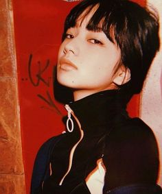 a woman with short black hair standing in front of a red wall