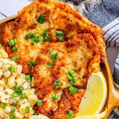 a wooden bowl filled with chicken, macaroni and cheese next to a lemon wedge