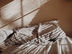 an unmade bed with white sheets and shadows on the wall