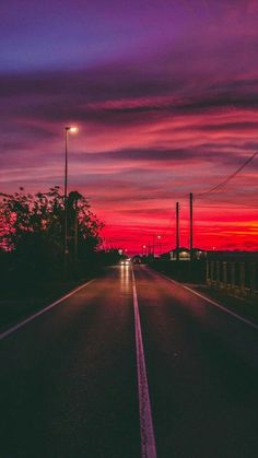 an empty road at night with the sun setting in the distance and some power lines on either side