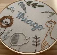 a close up of a embroidery on a wooden surface with animals and plants around it