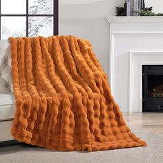 an orange blanket is on the floor in front of a white couch with a fireplace