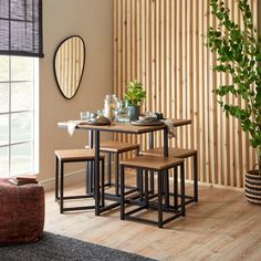 a dining table with four stools next to a potted plant and mirror on the wall