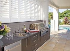 an outdoor kitchen with sink, grill and counter space next to the swimming pool area