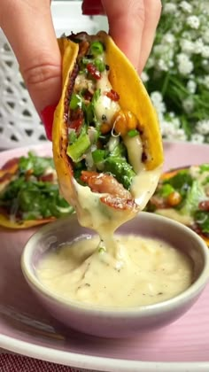 a hand holding a tortilla over a bowl filled with sauce and vegetables on a plate