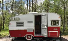 a red and white trailer is parked in the middle of some trees with its door open