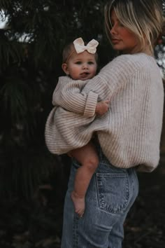 a woman holding a baby in her arms and wearing a sweater with a bow on it