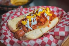 a hot dog covered in toppings sitting on top of a red and white checkered paper