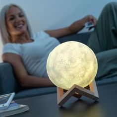 a woman sitting on a couch with a remote control in her hand and a moon lamp